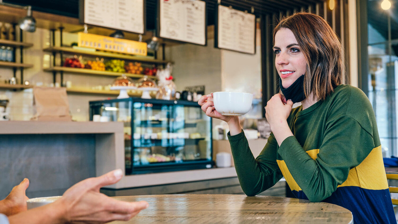 Woman in coffeeshop holding cup and mask