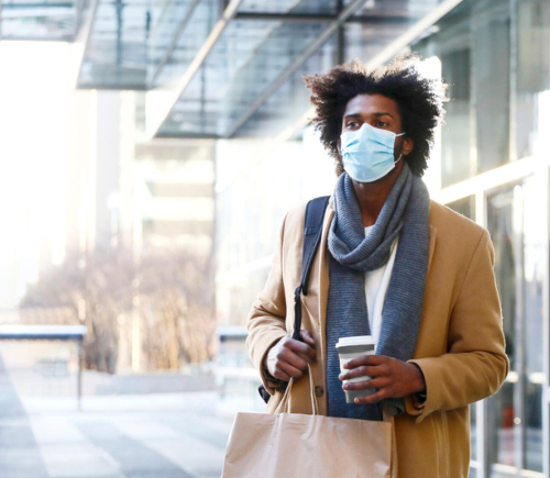 Masked man holding a cup of coffee and bags