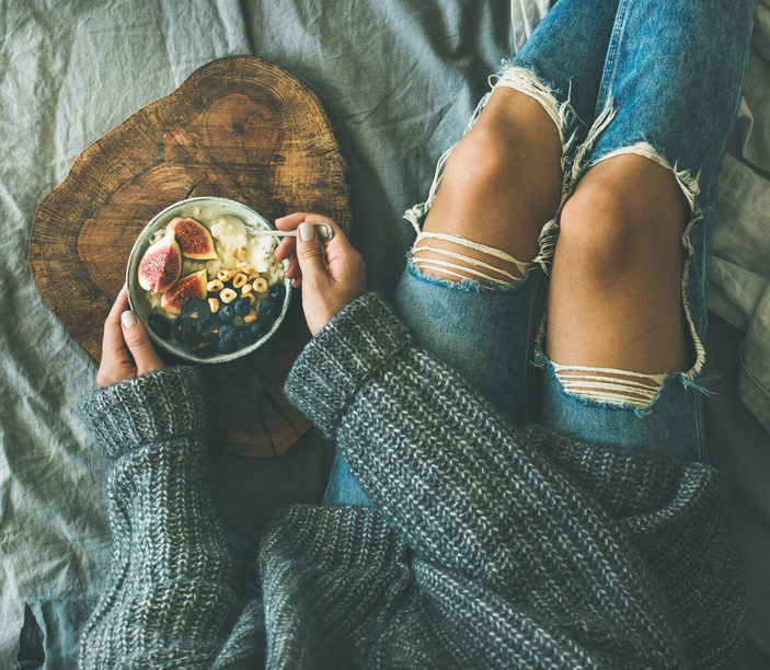 Person eating fruit from bowl on bed