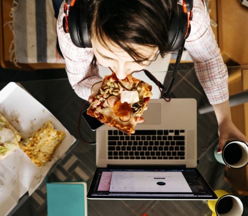 Person eating pizza at desk with computer