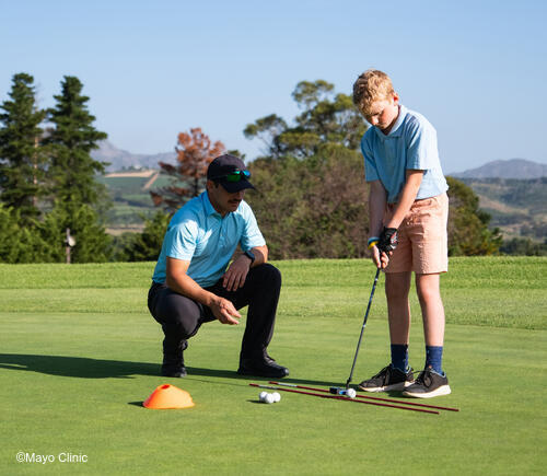 Adult man teaching young boy to golf.
