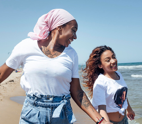 Two young women on the beach. They are laughing. One is wearing a headscarf.