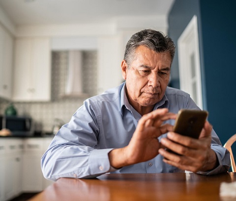 Older man sitting at kitchen table using smartphone.