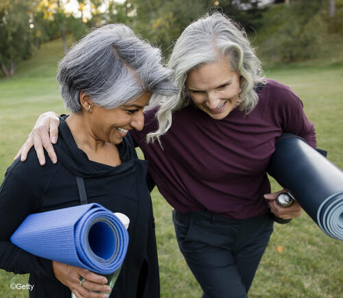 Women walking together outside carrying yoga mats.