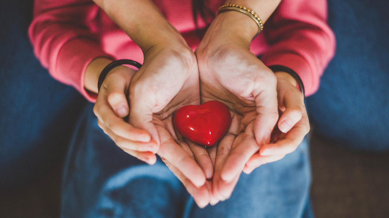 Womens' cupped hands hold a red heart shape