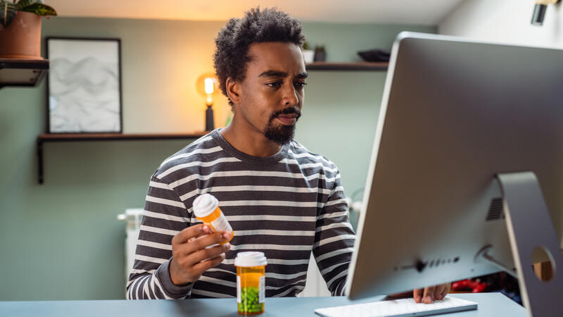 Man using desktop. Two prescription bottles on his desk. 