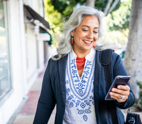 Woman with white hair smiling at her smartphone while walking outside