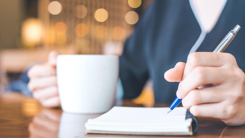 Woman making a list and drinking a cup of coffee