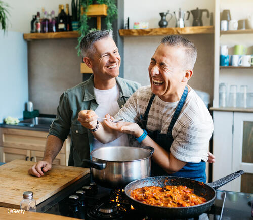 Two adult men cooking together happily.