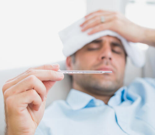 Man looking at thermometer while sick on the couch