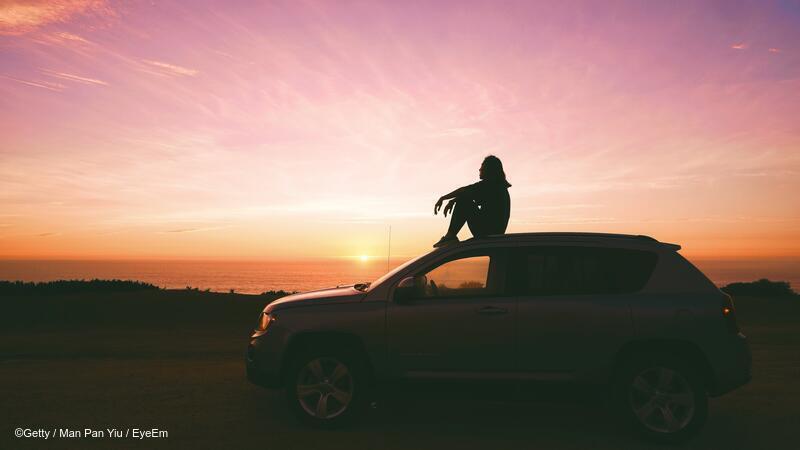 Person sitting on top of car near a body of water at dusk or dawn