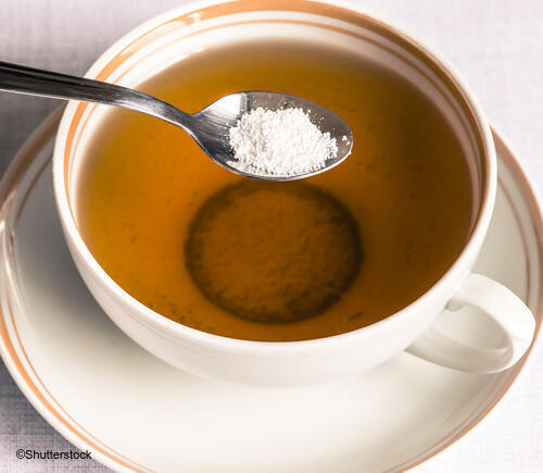 Spoonful of sweetener held over teacup. 