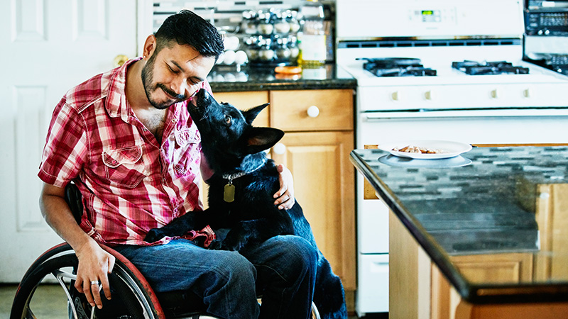 Man in a wheel chair receiving affection from his dog