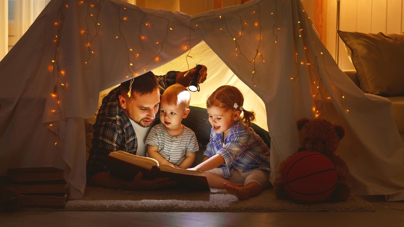 Parent reading book and indoor camping with with children