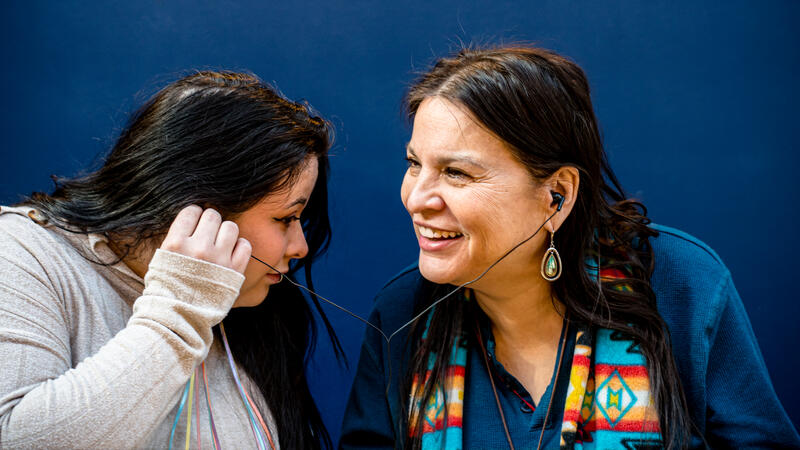 Two native women sharing earbuds