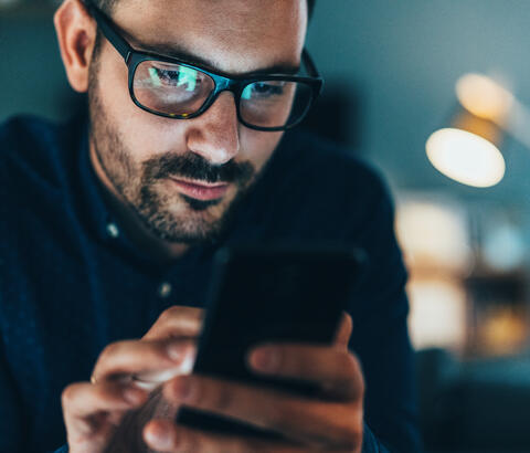 Man's face and glasses illuminated by smartphone