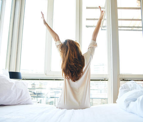 Adult woman sitting on edge of bed stretching