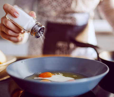 Person adding salt to eggs