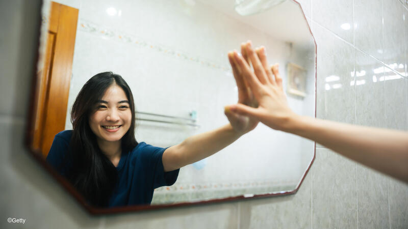 Young woman smiling at her reflection in the mirror