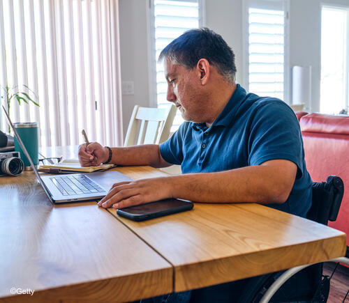 Male wheelchair user sitting at table using laptop.