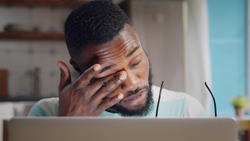 Man in front of computer rubbing his eye