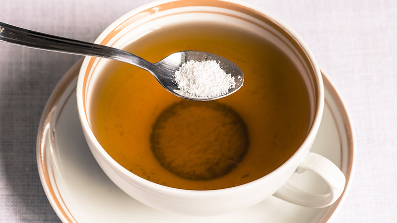 A spoonful of sweetener being added to a cup of tea