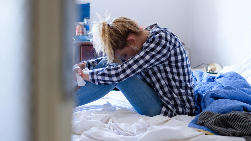 Woman sitting on bed with head in lap