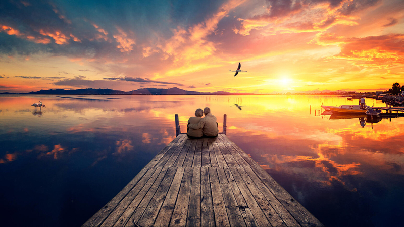 Couple sitting on the end of a doc watching a sunset