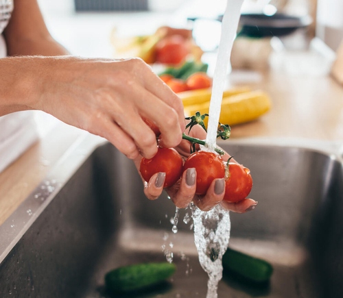 Woman washing tomatoes in kitchen sink