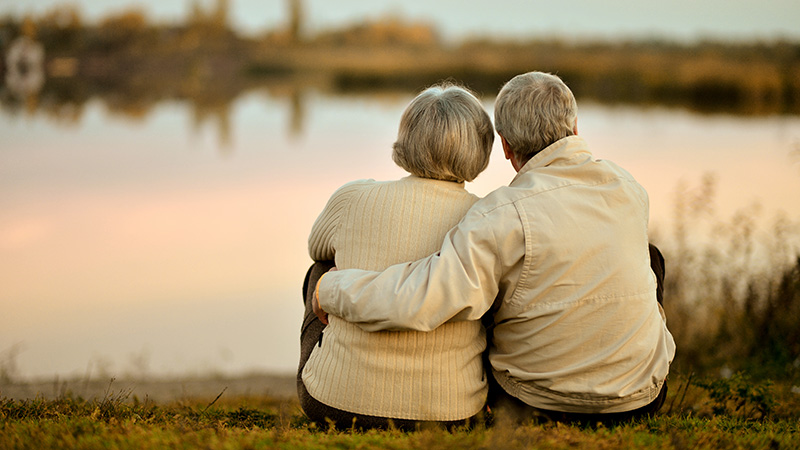 Man sitting with his arm around a woman on the bank of a lake