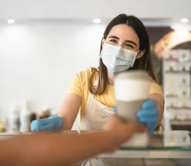 Masked barista handing coffee cup over counter