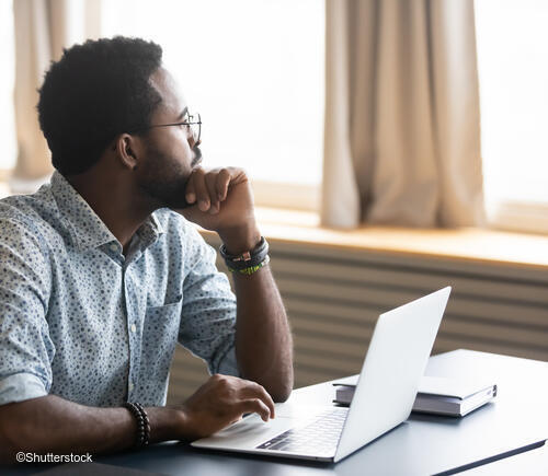 Adult man using laptop and looking out a window.