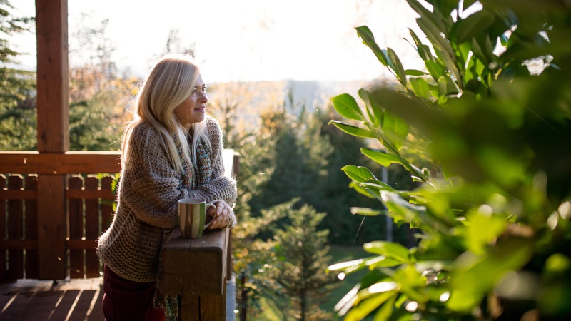 Woman on a deck in the summer with a cup of coffee looking out.