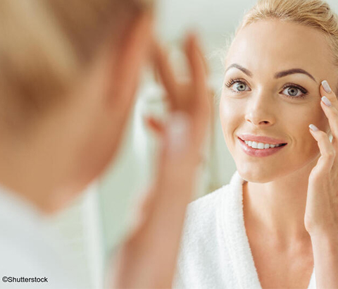 Woman applying skin care product in mirror.